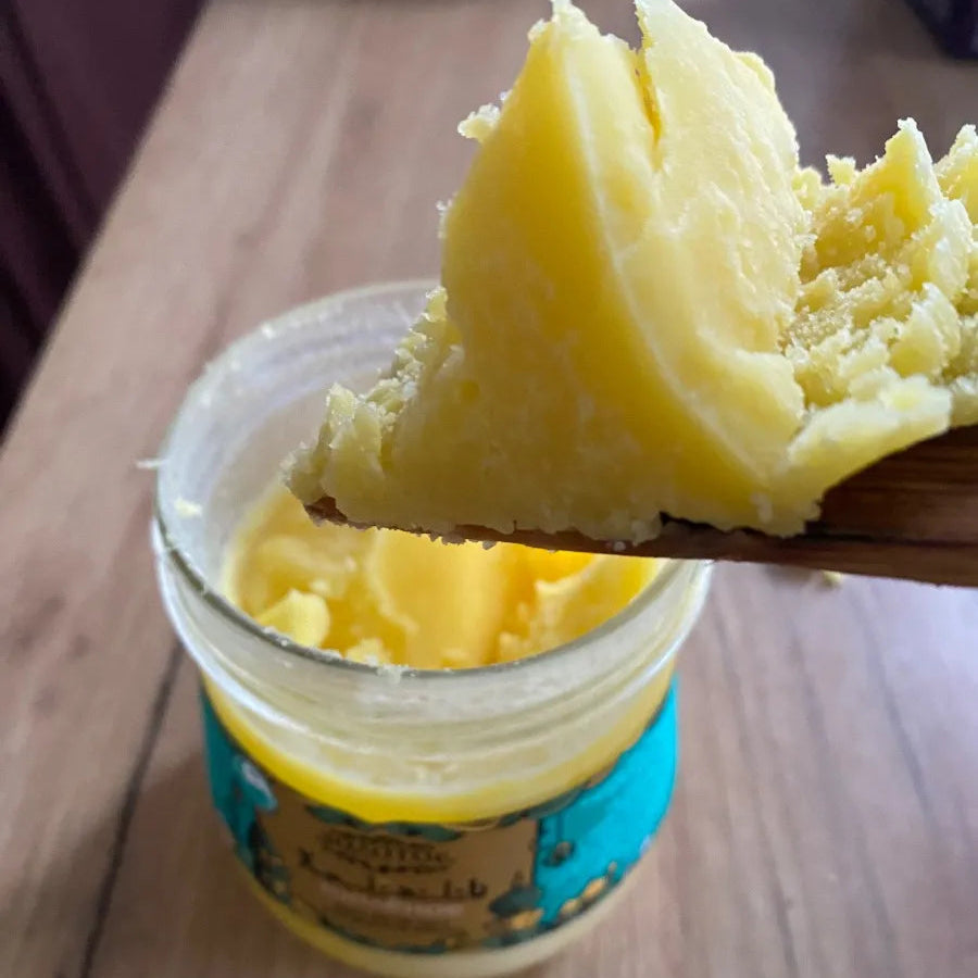 Wooden spoon lifting yellow cream out of a jar on a wooden surface